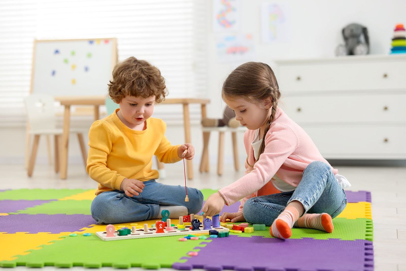 Kids are playing with the toys sitting on a mat in a classroom.